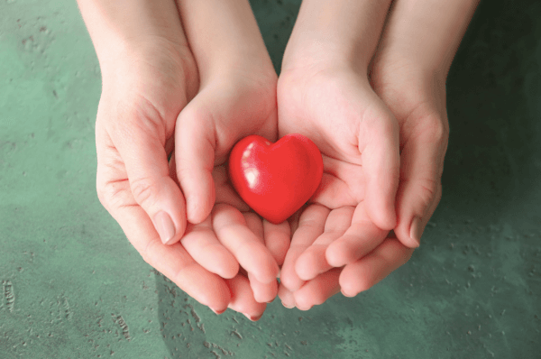 A child's hands on top of an adult's hands, holding a red heart
