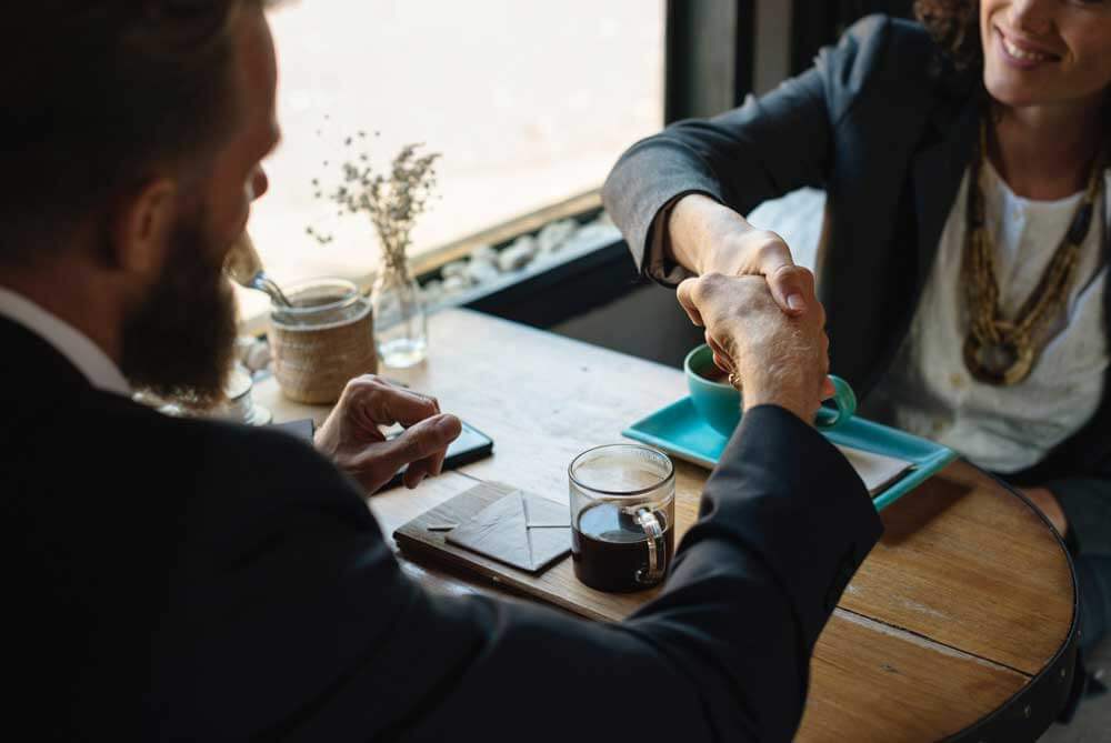 Man and woman in coffee shop shaking hands over business deal