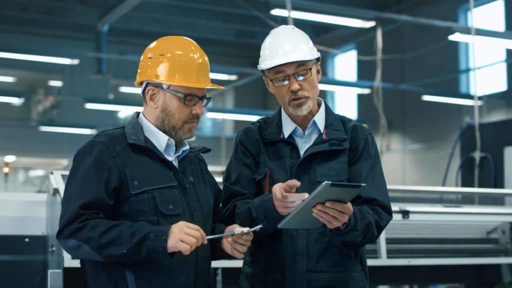 Two men in a factory wearing hardhats and talking