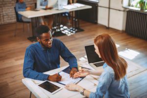 Man and woman sat on either side of a desk completing a form